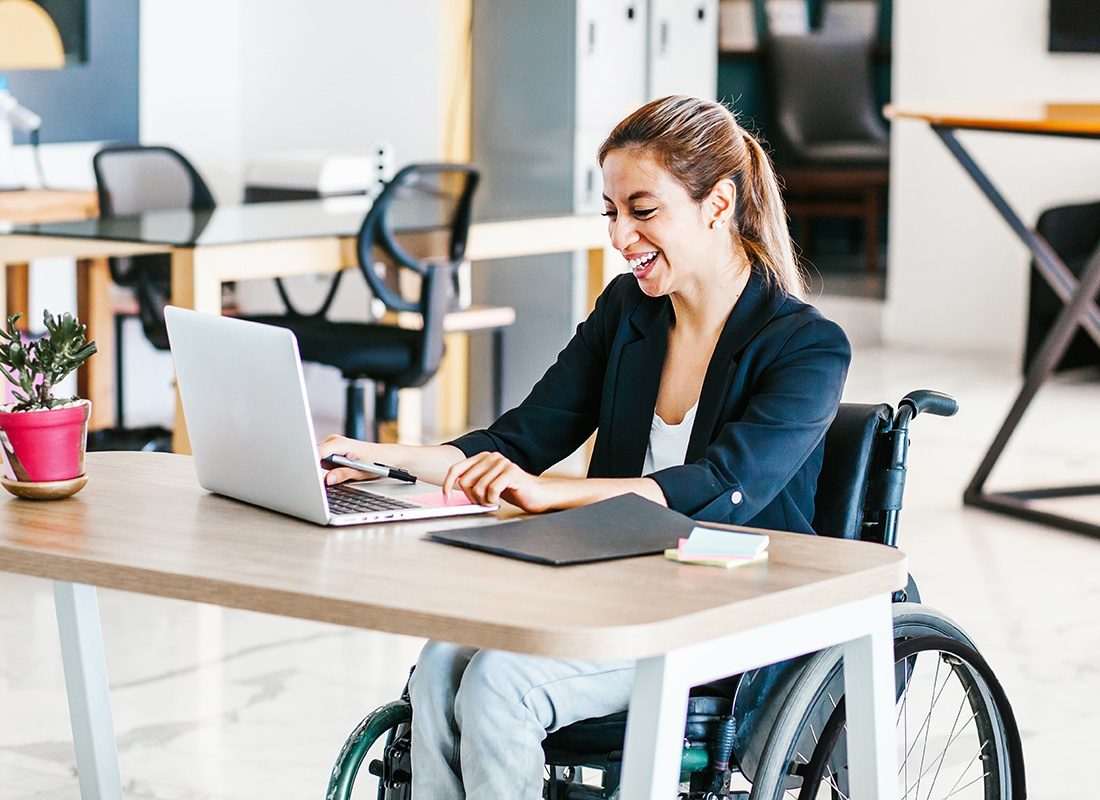 Read Our Reviews - Businesswoman in a Wheelchair at Her Desk, Smiling and Using a Laptop